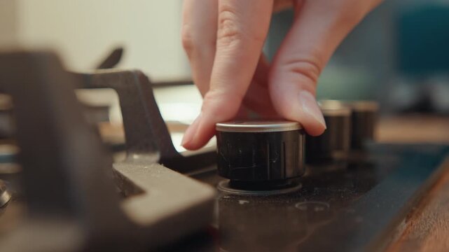 Hand tuning stove switch carefully. Close inspection of hand manipulating stove control in sunlight. Detailed view of hand precisely adjusting stove knob during meal preparation in sunny kitchen