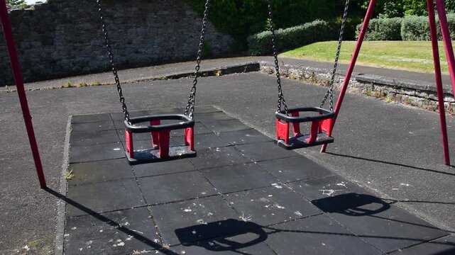 Close shot of two swings in a children's swing park on a bright summer day with greenery in the background