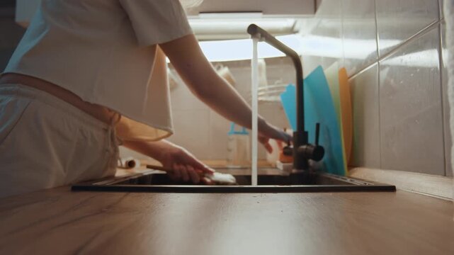 Hands at kitchen sink rinsing utensils, cooking prep with soft morning light, wooden counter, tile backsplash, colorful cutting boards, gentle faucet stream, calm domestic routine