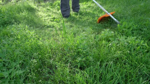 Person using a grass trimmer to cut overgrown grass in a lush green field, showcasing the tool's movement and effectiveness in maintaining the landscape