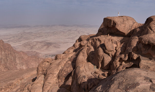 A bedouin in traditional clothing, long white robe with headscarf, in summit of Jebel Banat. Panorama of high mountains in national park Saint Katherine Protectorate. Authentic bedouin lifestyle.
