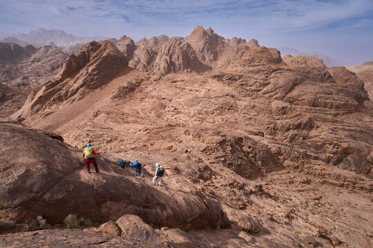 Group of hikers descends from summit in national park Saint Catherine Protectorate in Sinai, accompanied by bedouin guide. Panorama of red-hued peaks, forming layered ridges that fade into the horizon