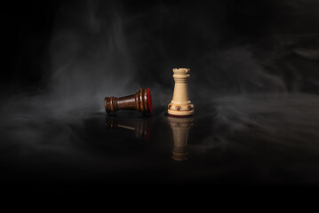Standing chess rook facing a fallen rook on a dark smoky background, symbolizing rivalry, victory, defeat, strategy, conflict, leadership, pressure and high‑stakes decision‑making. © Artur