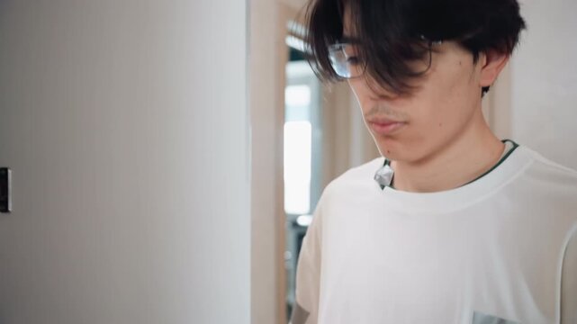 Inspecting closet before starting cleaning routine asian young man turns in narrow hallway, studies cabinet layout and hinge, spray bottle visible on counter, thoughtful planning for tidy makeover