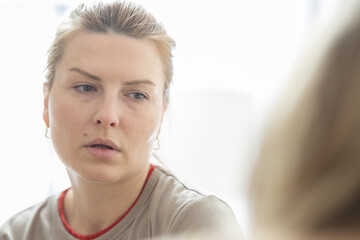 Fototapeta premium Female individual with light brown hair wearing a beige shirt, gazing thoughtfully while seated indoors with soft natural light illuminating the scene