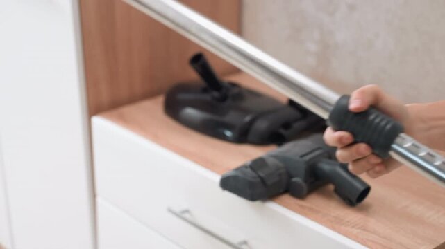 Long metal wand with nozzle attachment, hand aligning connector over tube, click connection and swivel joint closeup, prepping crevice head for upholstery and cabinet cleaning, modern kitchen