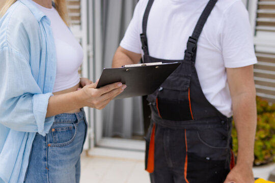 Woman reviewing service agreement on a clipboard with a repair technician at her home, discussing work details and confirming project scope before starting the job