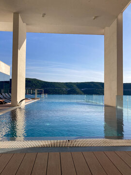 An infinity swimming pool overlooks a calm bay and lush green hills, capturing luxury travel and serenity at a sunny summer resort destination under a bright and clear blue sky