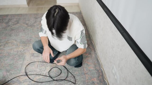 Individual neatly arranging cable loops. Someone carefully coiling extension cable on floor for storage purposes. Individual methodically organizing and coiling lengthy wire in cozy home environment