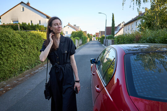 Woman in black jumpsuit standing next to a red car on a suburban street