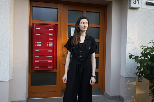 Woman in black jumpsuit standing in front of a modern building with red mailboxes