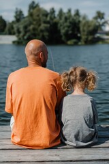 Obraz premium Man and child sitting on dock fishing by lake in afternoon sun