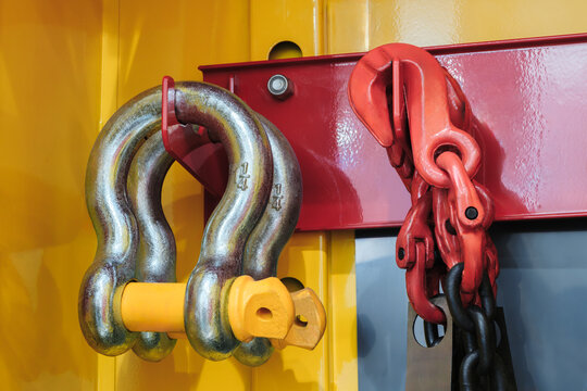 Close-up of industrial metal hardware, including chain and shackle. shackle features white pin and visible wear. Polished metal surfaces have brushed texture