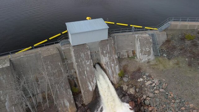 Water rapidly flowing out a sluice gate in an old dam. The view starts in close, and then pulls back and up to show a wide angle view that includes the river formed below the dam and surrounding area.