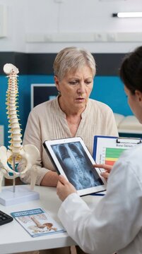 Senior health discussion: osteoporosis diagnosis, bone density, patient concern, doctor advise, spinal model, x-ray image, fragile structure, aged individual.