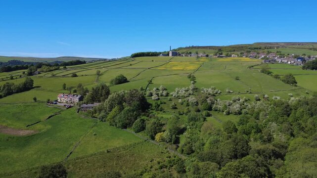 panoramic aerial drone view of the village of old town with the historic mill and houses surrounded by meadows and trees near hebden bridge