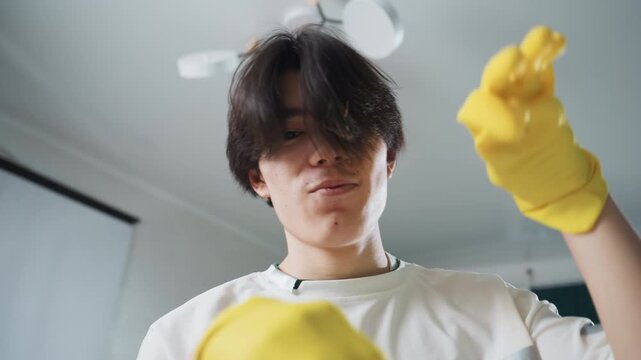 Preparing for household tasks diligently. Man in apartment getting ready for cleaning chores. Asian young man dressed in gloves preparing for house cleaning activities inside apartment