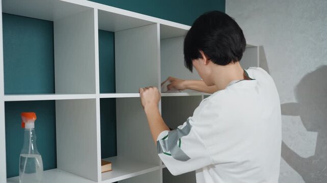 Person tidying cubby with supplies. Someone disinfecting and organizing storage areas meticulously. Individual using spray and cloth to carefully clean and organize cubby compartments
