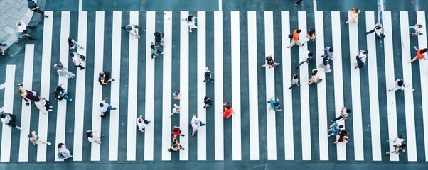 Obraz premium A bustling city crosswalk captured from above shows a crowd crossing bold zebra stripes. Colorful clothing and urban energy highlight modern pedestrian life.