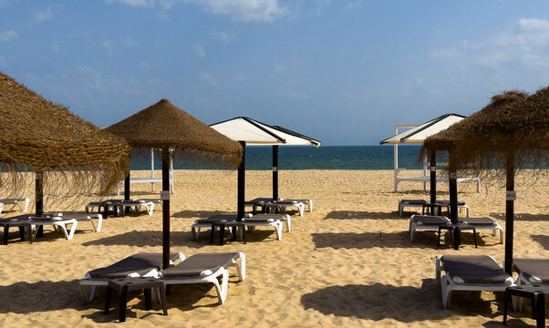 Scenic view of sandy beach with straw sunshades and white deck chairs. Resort. 