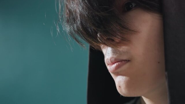 Frontal hoodie reveal intimate portrait young person pulling hood back hair falling over eyes soft teal background confident vulnerable expression closeup skin detail cinematic light