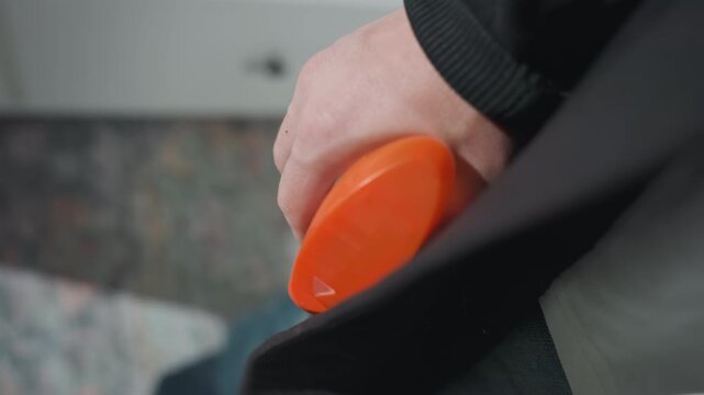 Hand using orange lint roller on coat pocket, indoor carpet background, closeup fabric pill removal, homeowner tidying wardrobe, gentle motion and textured detail for home cleaning and garment care