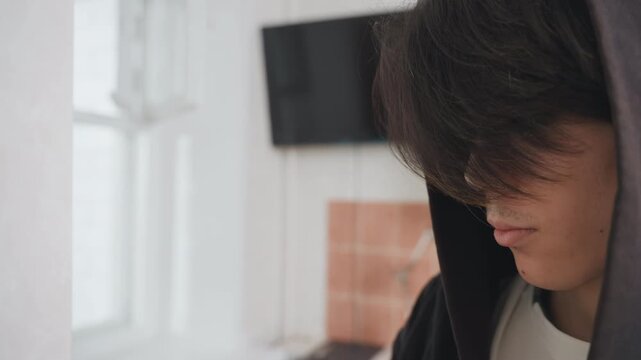 Asian teen organizing kitchen shelves, natural window light, tile backsplash and cabinets, focused expression, meal prep gesture, hands on cupboard, calm domestic routine, homecook narrative, intimate