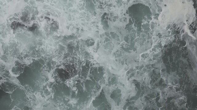 A drone view of waves crashing around Felgueiras Lighthouse platform beside a long seawall in misty coastal weather in Porto, Portugal
