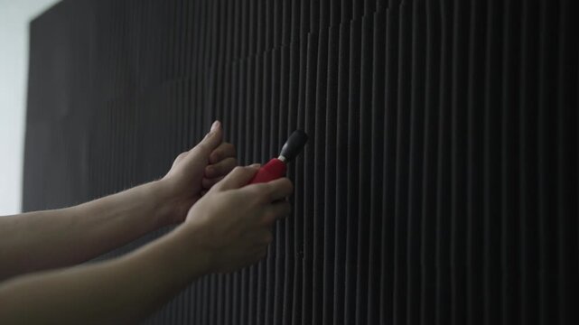 Hands of sound engineer testing dark acoustic foam panels with specialized equipment, ensuring optimal sound absorption and environment for recording, close-up, slow motion.