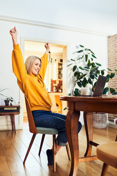 Woman celebrating success at laptop in home dining room