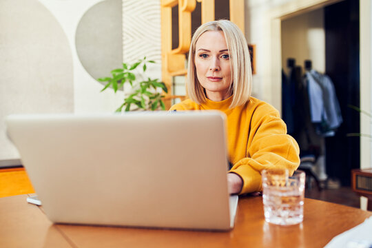 Woman working on laptop at dining table in modern home