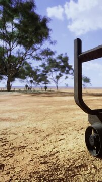 A piece of heavy equipment sits on dry land. The landscape features sparse trees and open space. The sun shines brightly in a mostly clear sky. It looks like a rural area with few signs of activity.