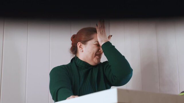Woman shows distress. Woman at residence manifests visible distress and discomfort symptoms. Female individual seated at her desk demonstrates obvious signs of distress and emotional discomfort