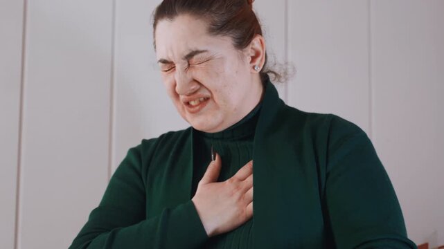 Woman clutching chest at home sudden chest pain, interior closeup showing grimace and shallow breathing, holding sternum, visible sweat and distress, urgent medical concern with implied paramedic