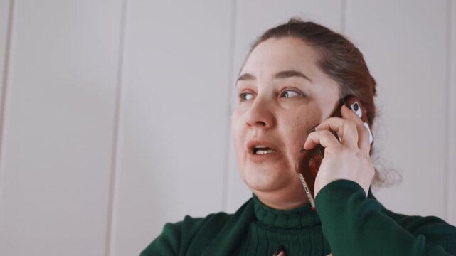 Woman pleads desperately. Woman urgently calls for aid. Frantic woman on phone seeking assistance immediately. An anxious woman presses her hand to her chest while speaking urgently