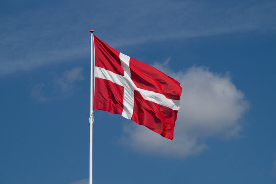 A Danish national flag, Dannebrog, waving gracefully in the wind against a vibrant, clear blue sky on a sunny day