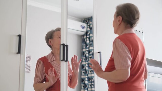 Happy elderly woman dancing and smiling while looking in the mirror