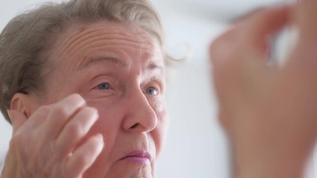 A cheerful old woman looks at her face in the mirror, close-up