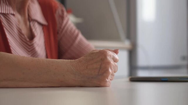 Close-up of an elderly woman slamming her fist on the table in anger