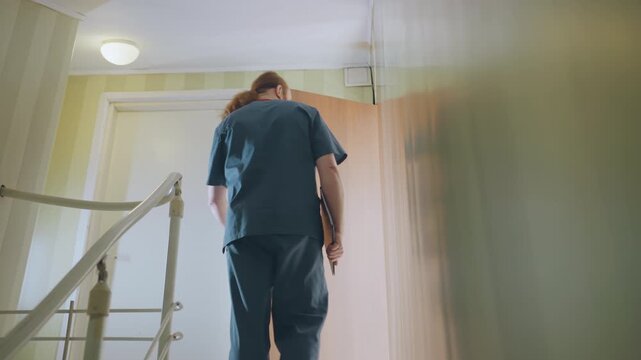 Black nurse descends home stairwell documenting, tablet in hand, stops at door to check notes, makes phone call to dispatch, gentle professional manner, warm corridor lighting and calm outreach vibe