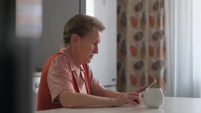 An elderly woman sits alone in the kitchen waiting for a call