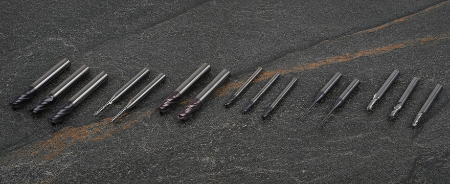 Arrangement of industrial drill bits and precision milling tools on dark stone texture background. Professional equipment for machining, engineering and metalworking tasks.