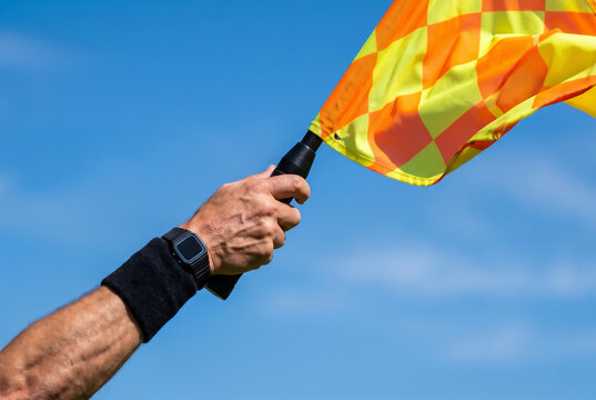 Assistant football referee's arm holding a checkered flag against a clear blue sky, signaling offside during a match.