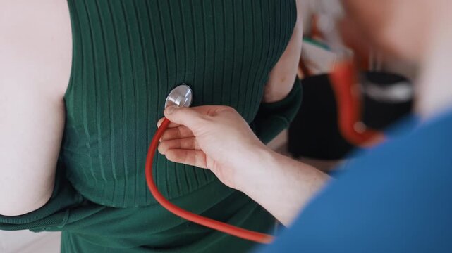 Stethoscope on back home visit white female patient in green sweater, paramedic listens for lungs with red tubing stethoscope, calm domestic interior bedside assessment, trustful interaction