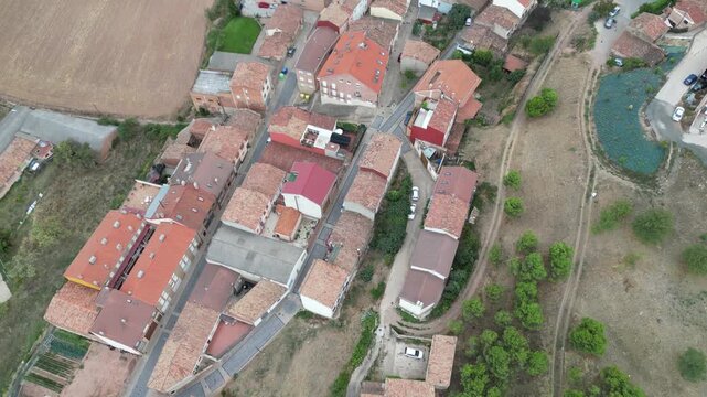 A drone view of narrow village streets lined with red-roofed houses beside dry fields and scattered greenery in Camino de Santiago, Navarrete, Spain