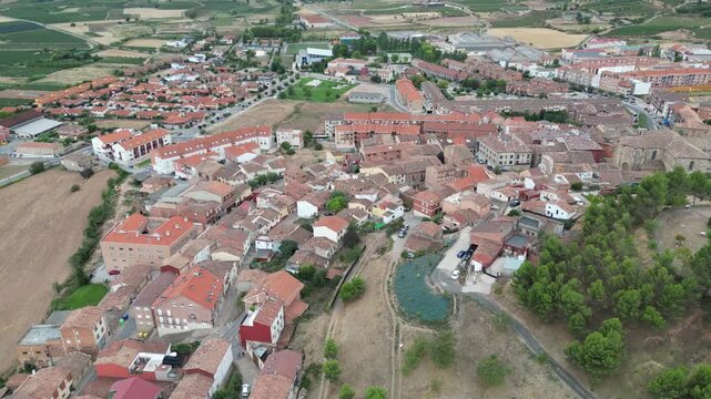 A drone view of a dense rural town with red rooftops, winding streets, open fields and clusters of trees in Camino de Santiago, Navarrete, Spain