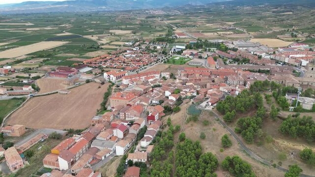 A drone view of a rural town with red-roofed houses, open fields and surrounding hills in Camino de Santiago, Navarrete, Spain