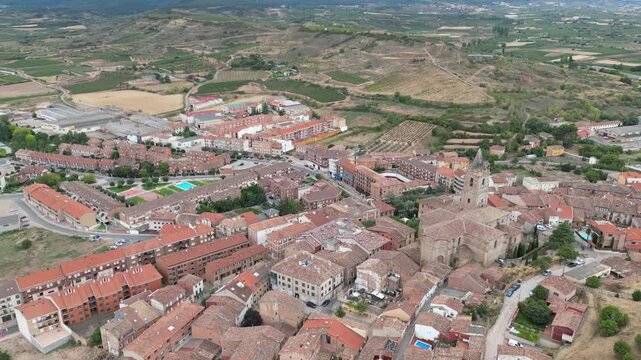 A drone view of a rural town with red-roofed houses, open fields and surrounding hills in Camino de Santiago, Navarrete, Spain