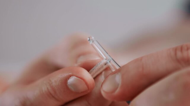 Closeup hands breaking glass ampoule, caregiver prepping medication at home, gentle lighting, neutral background, steady fingers opening sealed vial and measuring dosage with precision