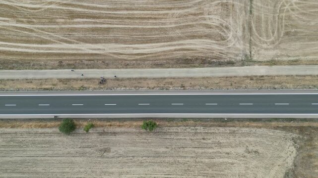 A drone view of straight rural road and path with walkers and cyclist between harvested fields with soft textures and sparse greenery in Spain
